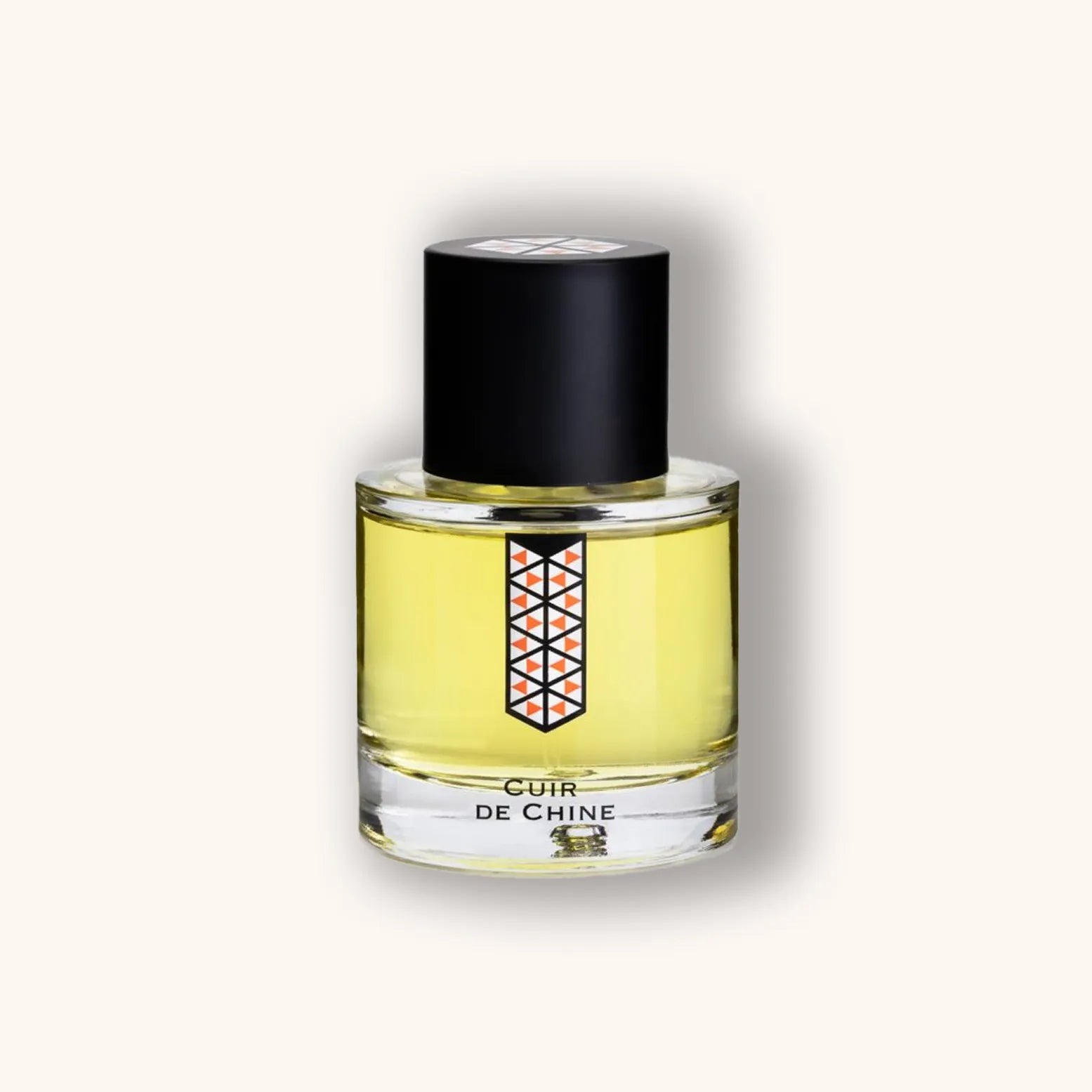 A sleek bottle of 'Les Indémodables Cuir de Chine' perfume, featuring a geometric label and a classic black cap, filled with a golden-yellow fragrance. The design exudes elegance and sophistication.