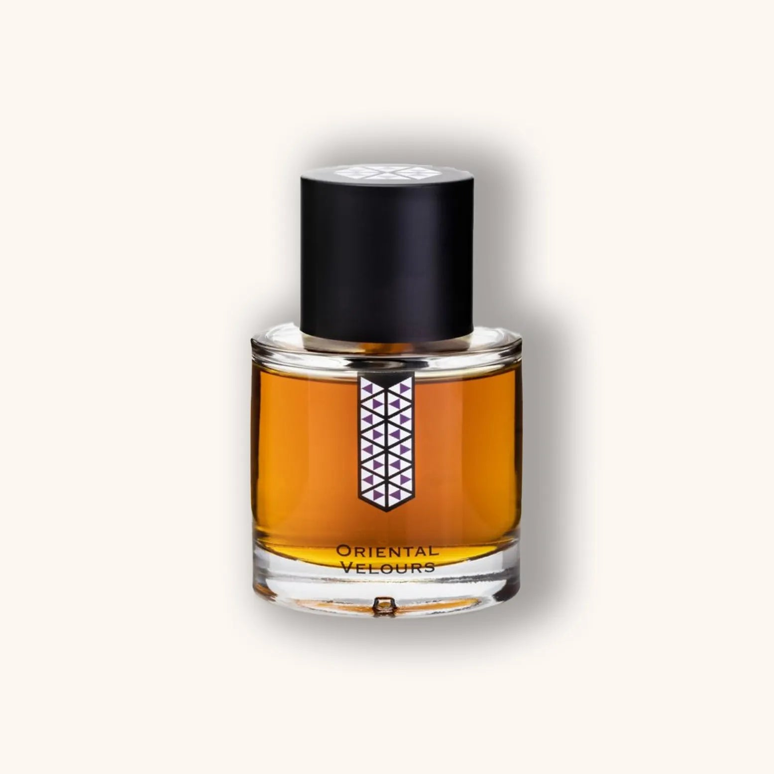 Alt text: Elegant bottle of 'Les Indémodables Oriental Velours' fragrance, featuring a geometric label and a dark cap, with a rich amber liquid visible inside.