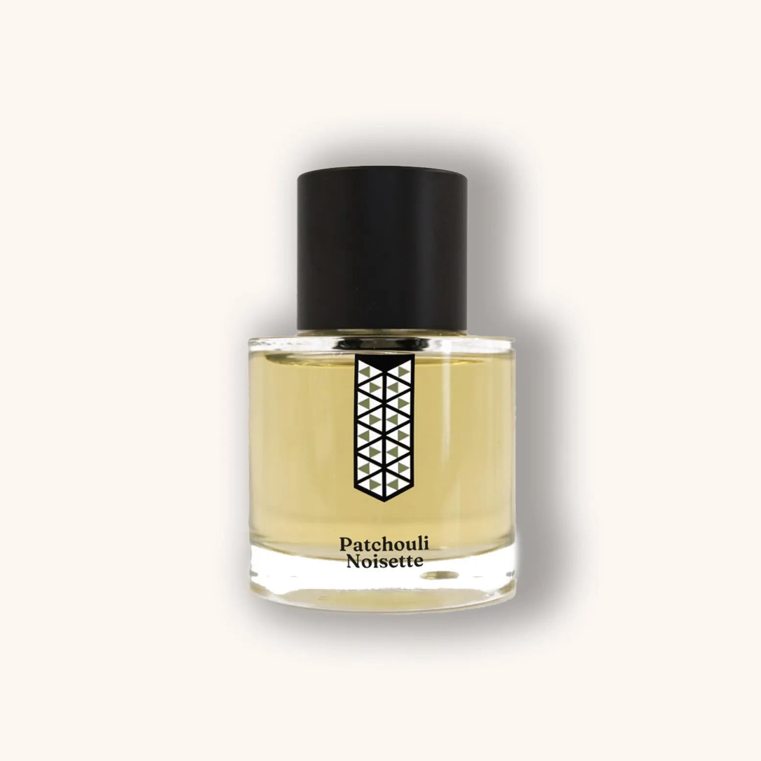 Alt text: A clear glass bottle of Les Indémodables Patchouli Noisette fragrance, featuring a geometric design label and a sleek black cap, showcasing a light amber liquid.