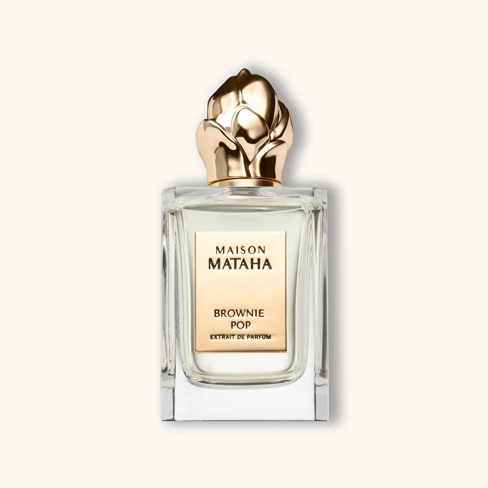 Alt text: A stylish glass perfume bottle labeled "Maison Mataha Brownie Pop," featuring an elegant gold floral cap and a soft beige label. The fragrance is categorized as an extrait de parfum.