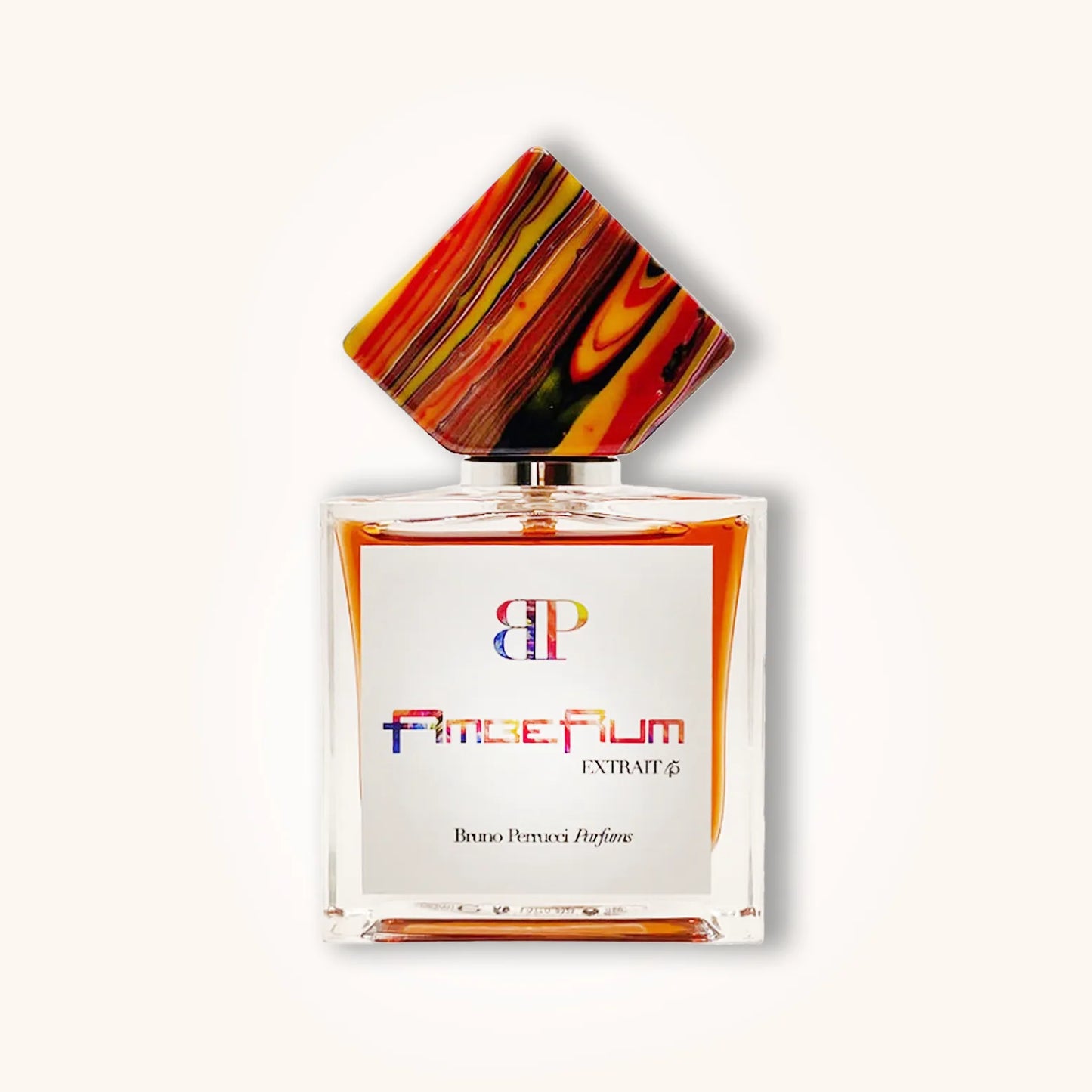 A stylish bottle of Bruno Perrucci AmbeRum, featuring a distinctive colorful geometric cap atop a clear glass container with a white label. The fragrance is presented as an extrait, showcasing an elegant and artistic design.