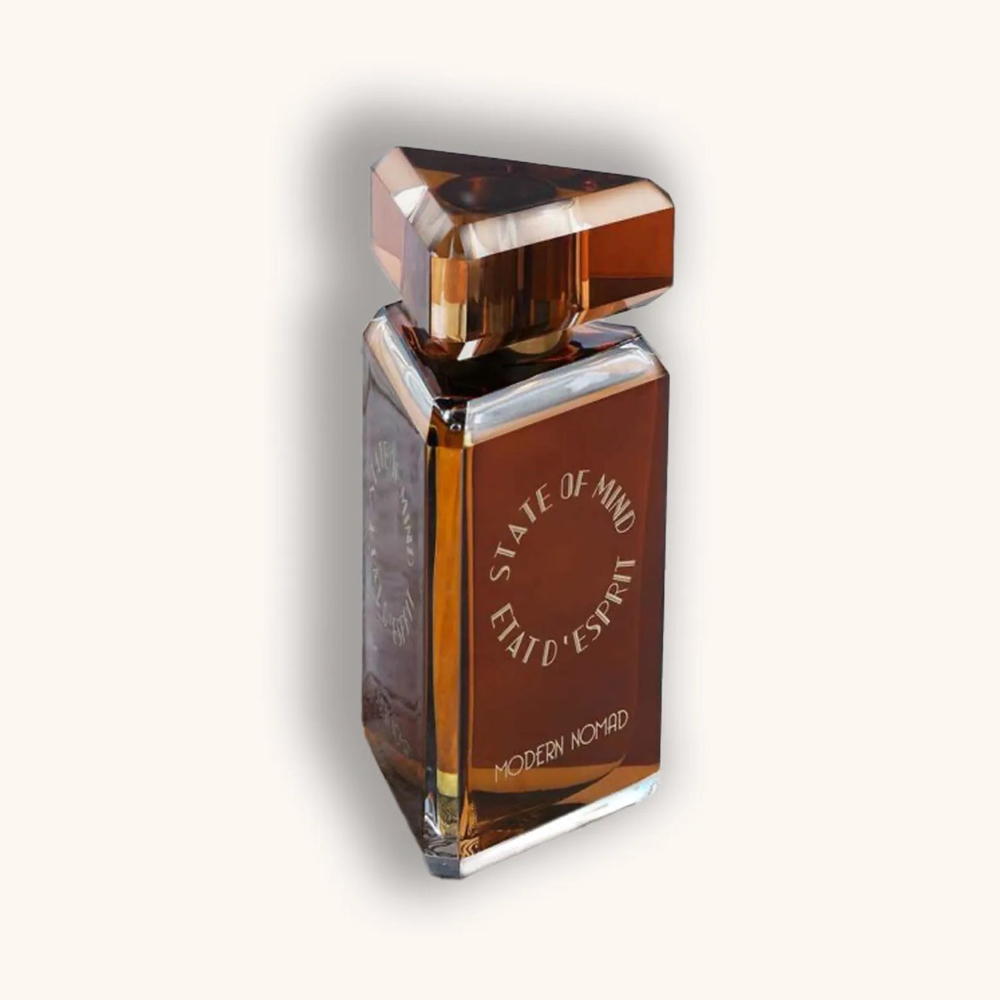 Alt text: A sleek, modern perfume bottle titled "State of Mind Modern Nomad," featuring a geometric design with a warm amber hue and a distinctive triangular cap. The bottle is elegantly displayed against a soft, neutral background.