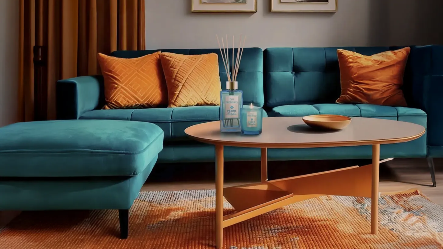 Blue sofa with orange cushions and a wooden coffee table with Perris Portofino Candle in a living room setting.