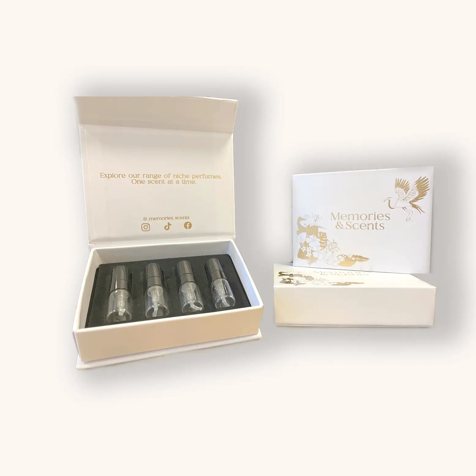 An open 'Memories & Scents Review Box' showcasing four perfume samples in elegant glass vials, set against a stylish background. The box features a gold and white design with the brand name prominently displayed on the exterior.